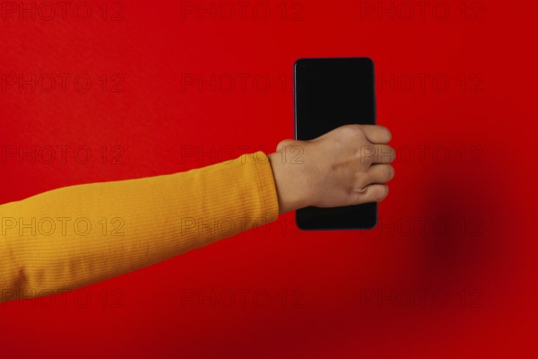 Crop hand of anonymous male demonstrating cellphone black screen against red background