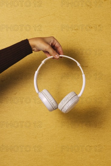 Crop hand holding headphones on golden background