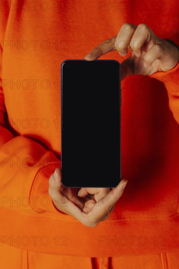 Crop anonymous female in orange casual clothes showing smartphone with empty screen
