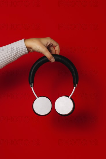 Crop anonymous person holding wireless headphones over red background