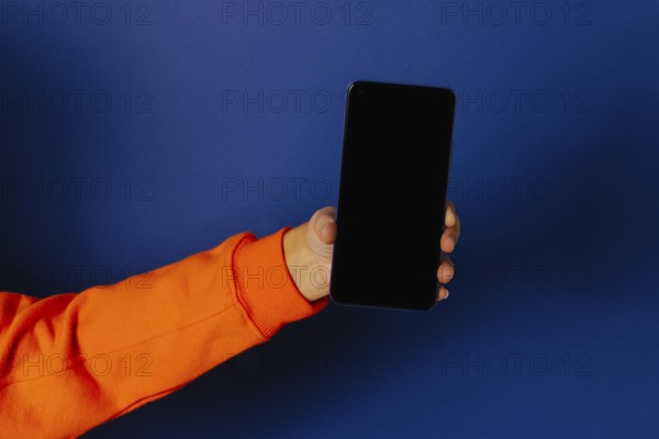 Crop hand of anonymous person holding smartphone with black screen against blue background