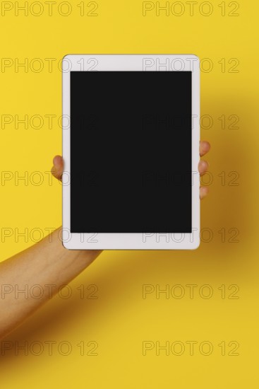 Crop hand of anonymous male demonstrating tablet black screen against yellow background