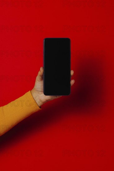 Crop hand of anonymous male demonstrating cellphone black screen against red background