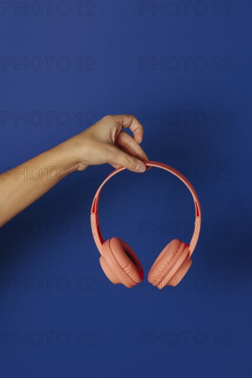 Crop anonymous person holding wireless pink headphones over blue background
