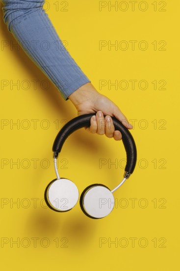 Crop hand holding headphones on yellow background
