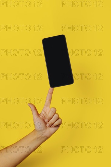 Anonymous person balancing a mobile phone on yellow background
