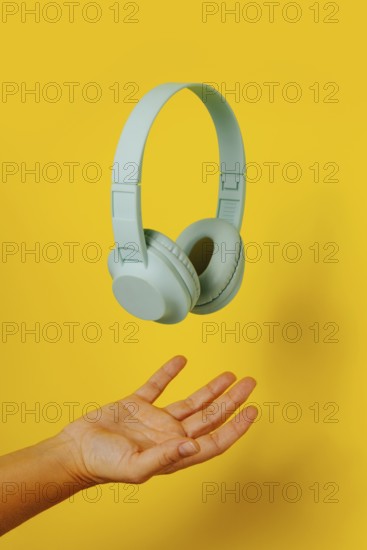 Crop anonymous person holding levitating headphones on yellow background