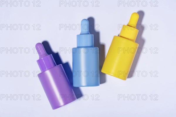 Top view of three vibrant-colored cosmetic serum bottles in purple, blue, and yellow neatly arranged on a clean white background, casting soft shadows
