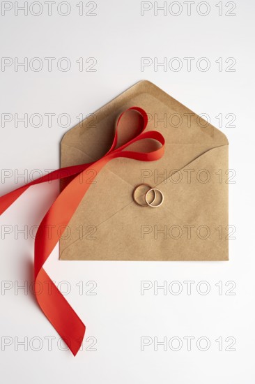 Top view of gold wedding rings placed on a brown envelope, tied with a vibrant red ribbon, suggesting a romantic concept perfect for Valentine's Day
