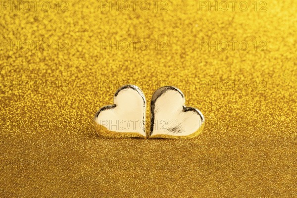 Two golden heart-shaped objects set against a shimmering golden backdrop, ideal for St. Valentine's Day themes