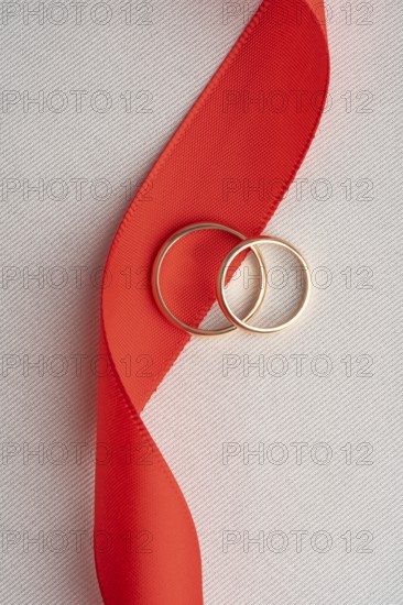 Two elegant gold wedding rings lying on a bold red ribbon, captured on a textured white backdrop. A perfect image symbolizing love and marriage, ideal for St. Valentine's Day themes