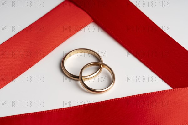 Two gold wedding rings lie elegantly on a vibrant red satin ribbon, symbolizing romance and commitment