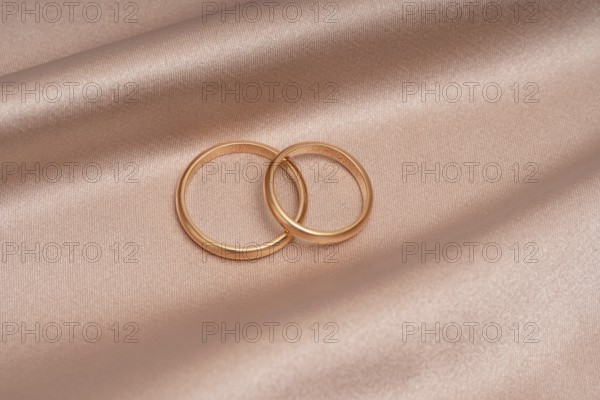 Two gold wedding bands gracefully overlap atop a blush satin surface, symbolizing eternal love and commitment