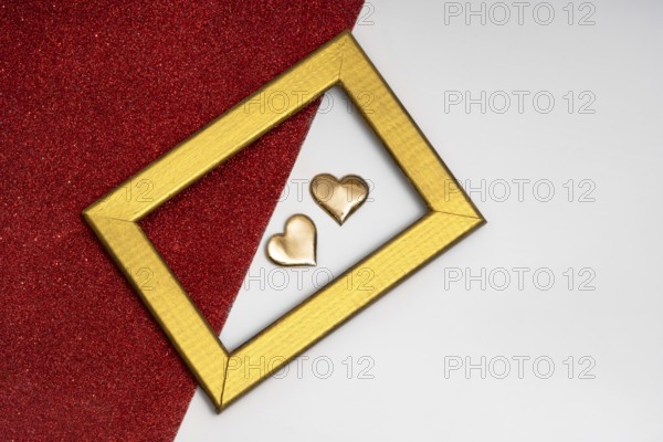 Two golden heart-shaped objects and a rectangular golden frame on a red glittery background, symbolizing love and romance