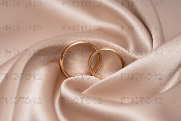 Two golden wedding rings interlocked, symbolizing unity and love, rest gently on a luxurious satin backdrop