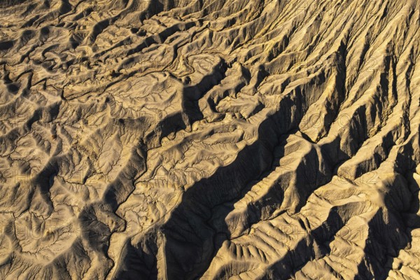 Aerial view of golden desert textures at Caineville Mesa, Utah. Features notable ridges and shadows, enhancing the unique geological formations and patterns