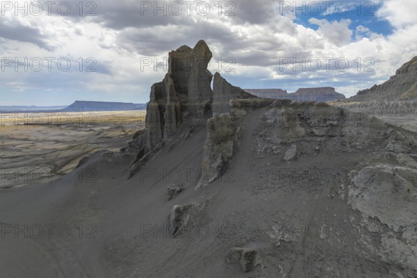 A dramatic view of towering rock formations in a vast desert landscape in Hanskville, Utah. The sky, filled with clouds, contrasts with the rugged terrain, creating a sense of grandeur and isolation
