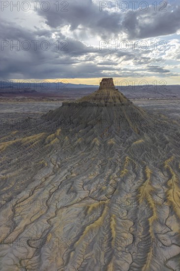 Aerial view of a rugged desert landscape, with intricate textures and eroded landforms under a cloudy sky in Hanskville, Utah. Dawn light bathes the scene, casting shadows on the terrain of USA