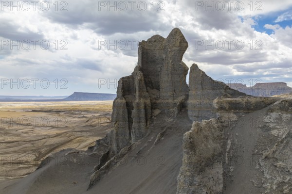 A towering rock formation emerges from the expansive desert landscape under a cloudy sky in Hanskville, Utah. The rugged terrain and dramatic cliffs add depth to this breathtaking scene of USA
