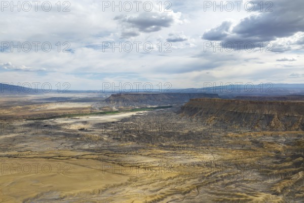 Aerial view of a rugged desert landscape under a dramatic, cloud filled sky in Hanskville, Utah. The image features eroded terrains, cliffs, and expansive vistas, highlighting nature raw beauty