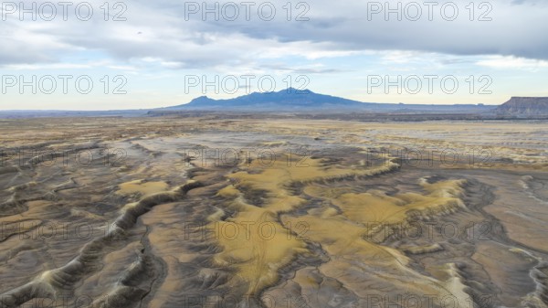 Aerial view of vast desert plains in USA with undulating terrain and patches of sand dunes, framed by a distant mountain range under a cloudy sky in Hanskville, Utah