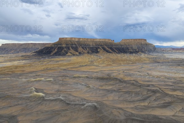 A breathtaking view of a desert plateau rising under a vast, cloudy sky, showcasing layers of sediment and earth tones, evoking a sense of timelessness and natural wonder in Hanskville, Utah