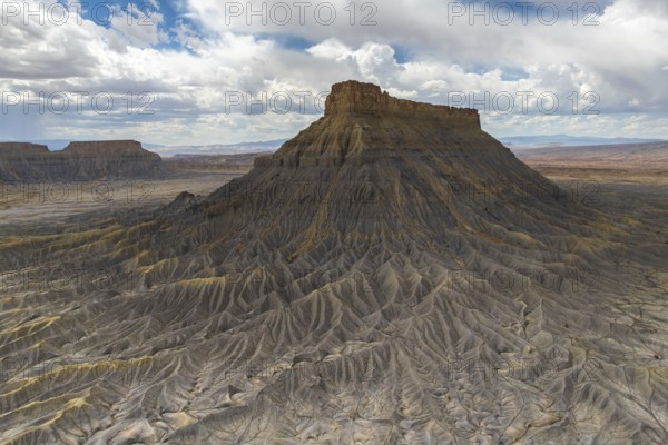 A striking aerial view of a weathered plateau with deep ridges and a barren landscape, under a dramatic sky filled with clouds, capturing the rugged beauty of nature in Hanskville, Utah