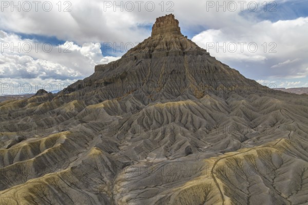 A striking desert mesa rises prominently against a backdrop of expansive clouds, showcasing intricate erosion patterns and layers that reveal the ancient geological history in Hanskville, Utah