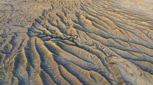Aerial view of Caineville Mesa's rugged landscape. Eroded valleys and golden hues capture the desert's intricate textures, creating a stunning natural pattern in Utah's wilderness