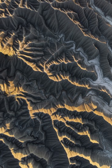 Aerial photo capturing golden desert textures and intricate patterns of Caineville Mesa, Utah. The sunlight casts dramatic shadows, highlighting the rugged terrain