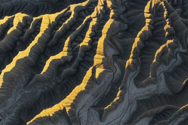 Aerial view of Caineville Mesa, Utah, showcasing dramatic ridges illuminated by golden sunlight. The textured landscape captures the essence of desert beauty and erosion
