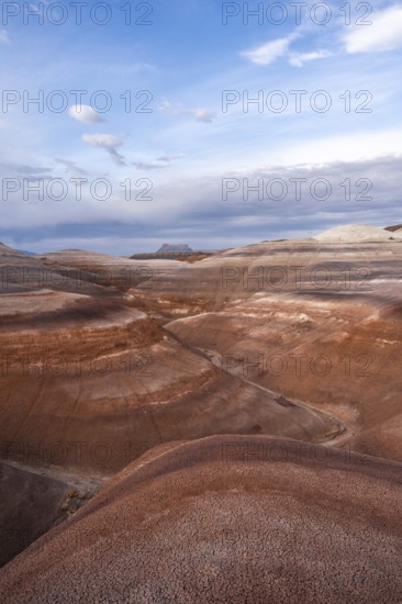Panoramic view of Hanksville's bentonite hills in Utah, showcasing layers of vibrant earth tones under a vast blue sky, embodying the serene beauty of desert landscapes