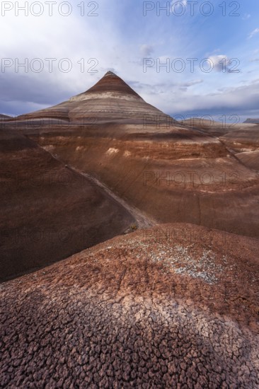 A stunning view of Hanksville Bentonites in Utah showcases layered, multicolored formations under a dramatic sky. The cracked earth texture adds depth to this arid landscape