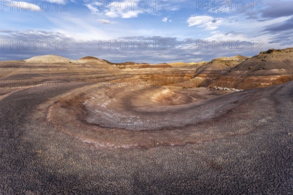 Dramatic aerial view of Hanksville Bentonite Hills in Utah, showcasing colorful, layered rock formations under a vast, partly cloudy sky, highlighting nature's artistry