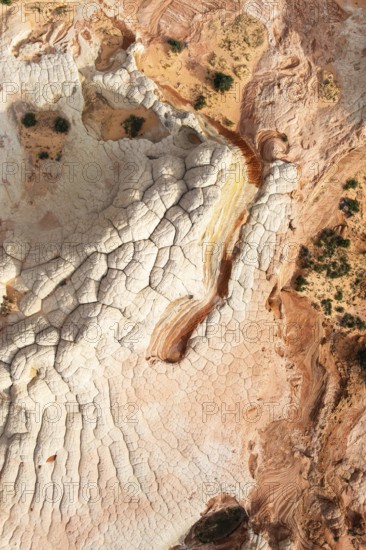 Aerial view capturing a desert landscape with rock formations, showcasing natural textures and earthy tones in White Pocket. Sparse greenery contrasts with red and white patterns in Arizona, USA