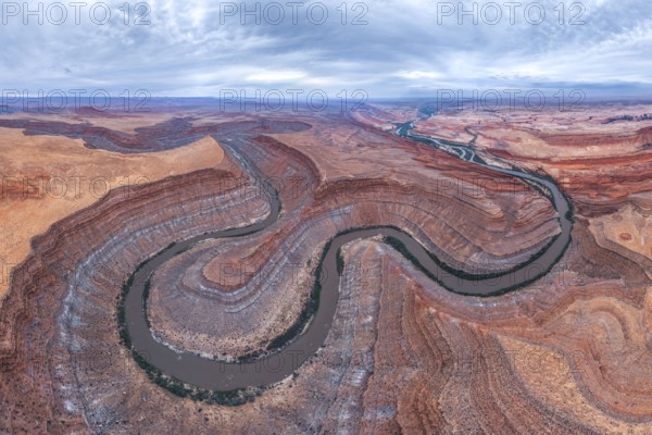 Captivating aerial view of a river winding through the dramatic, layered San Juan canyon. The contrasting colors of the rock formations and water create a stunning natural landscape in Utah, USA