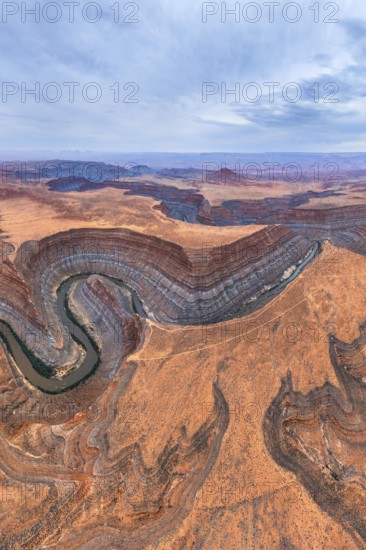 Aerial view of San Juan canyon with a winding river cutting through the arid desert landscape. The layered rock formations display earthy tones under a wide, partly cloudy sky in Utah, USA