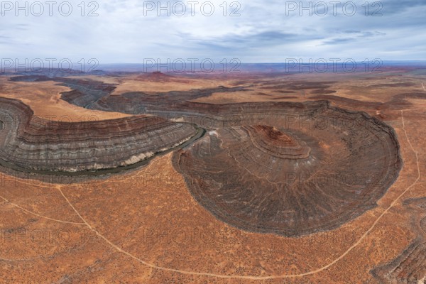 An aerial view showcases a river elegantly meandering through layered rock formations in a vast San Juan canyon landscape, under a serene blue sky, highlighting natural beauty and geological wonders