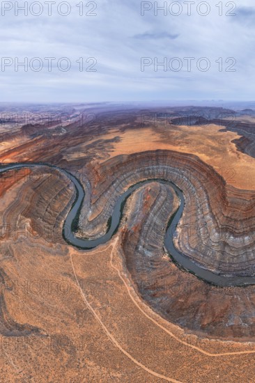 An aerial view captures a winding river cutting through a desert in San Juan canyon, showcasing layered rock formations and contrasting earth tones under an expansive sky in Utah, USA
