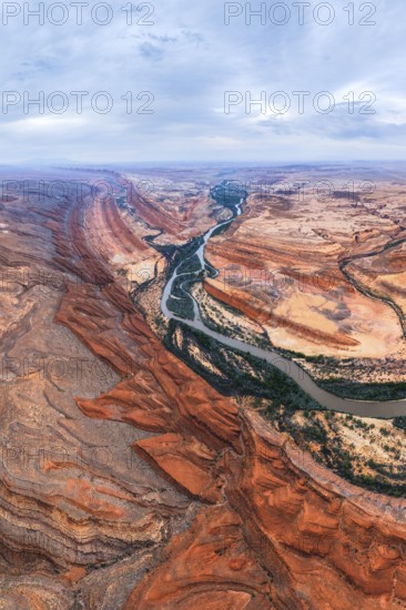 Aerial view showcasing a vibrant San Juan canyon with a winding river flowing through it. The scene captures the natural beauty of the red rocks and expansive landscape under a blue sky in Utah, USA