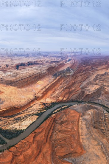 Captivating aerial view of a sprawling San Juan canyon with layered rock formations and a meandering river under a partially cloudy sky, showcasing nature rugged beauty in Utah, USA