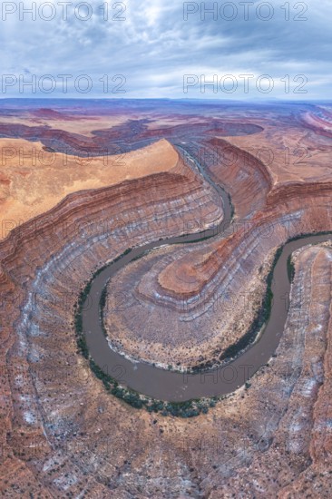A stunning aerial view captures a serpentine river winding through layered rock formations in a rugged desert landscape, showcasing nature artistry and timeless beauty in Utah, USA