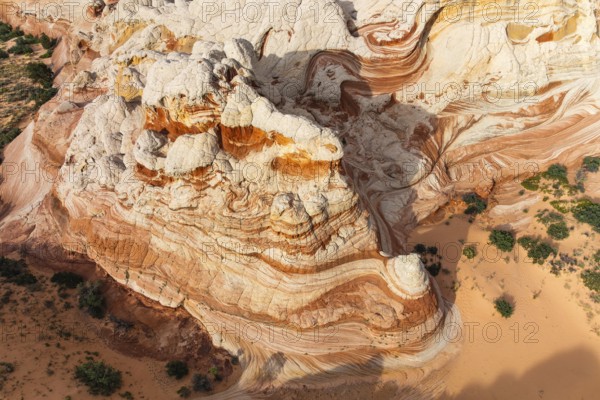 Aerial view overlooking colorful, swirling rock formations in a desert landscape in White Pocket. The geological structures exhibit intricate patterns and hues against sandy terrain in Arizona, USA