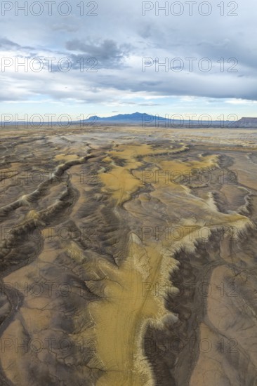 Aerial view of an expansive desert terrain featuring rugged formations and soft sand hues in Hanskville, Utah. A distant mountain range contrasts with the sky, creating a dramatic horizon in USA