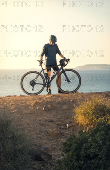 Male cyclist holding his road bike and gazing at the sea during sunset in Zahara de los Atunes, Cadiz