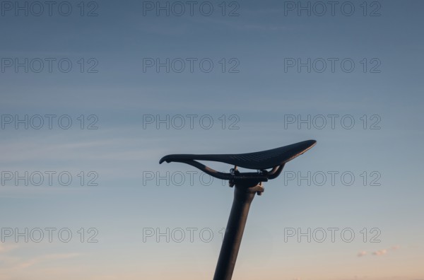 A minimalist silhouette of a bicycle saddle seat set against a soft sunset sky. The image evokes a sense of peace and solitude, capturing the simplicity and essence of cycling