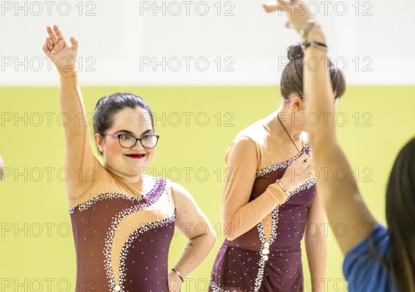 A confident gymnastic whit disability in colorful costumes perform in a bright studio. One person exhibits confidence and joy, raising an arm with a smile, highlighting inclusivity and passion