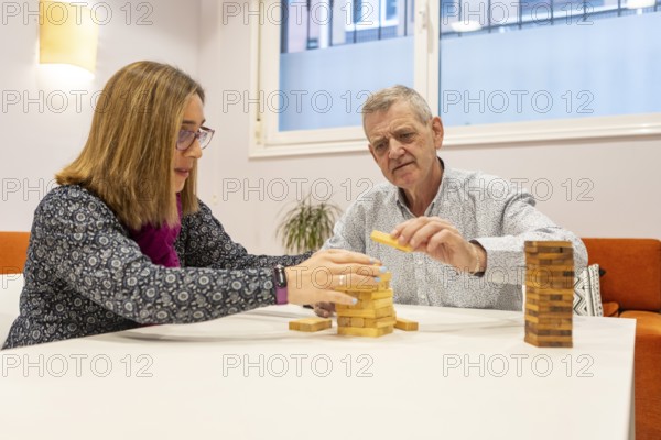 A couple with intellectual disabilities play a block stacking game together at a table of a supervised home. Their expressions show concentration and enjoyment