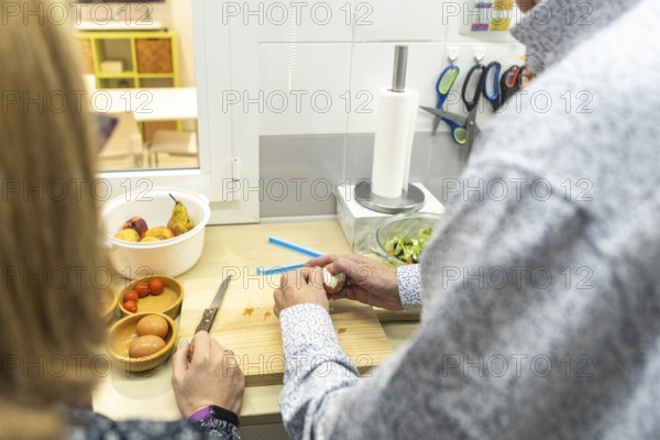 A couple with intellectual disabilities is preparing a healthy meal in a modern kitchen of a supervised home. Fresh ingredients like eggs, tomatoes, and fruit are visible