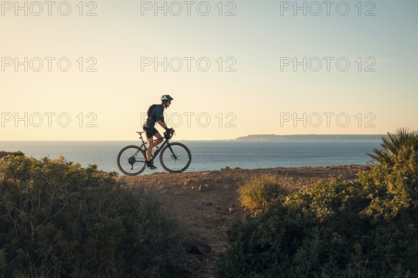 A young male cyclist rides along a scenic coastal path in Zahara de los Atunes, Cadiz, with the ocean and cliffs in the background
